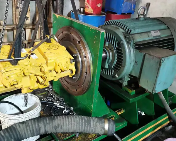 Bright workshop scene with a yellow hydraulic pump component attached to a large teal motor, warm industrial atmosphere with hanging tools, golden and teal tones.