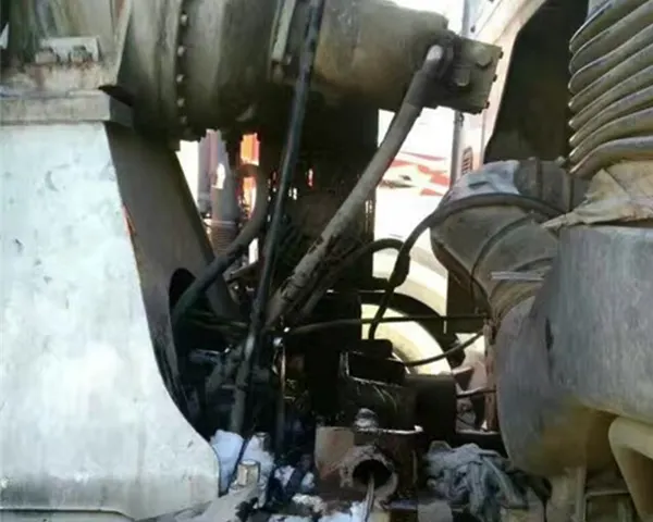 Close-up of heavy machinery undercarriage with hoses, pipes and metal housing, moody rust and charcoal tones softened by ambient workshop light.